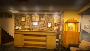 A reception area with a wooden counter, a stone wall with framed pictures, a small shrine, and a couch. - P K Rresidency (Madurai)