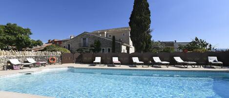 A swimming pool with lounge chairs and a lifebuoy, surrounded by stone walls and a tall tree.