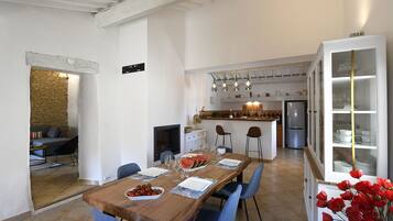 Comedor con una mesa de madera dispuesta para cuatro, sillas azules, una cocina al fondo y un aparador de vidrio con vajilla.