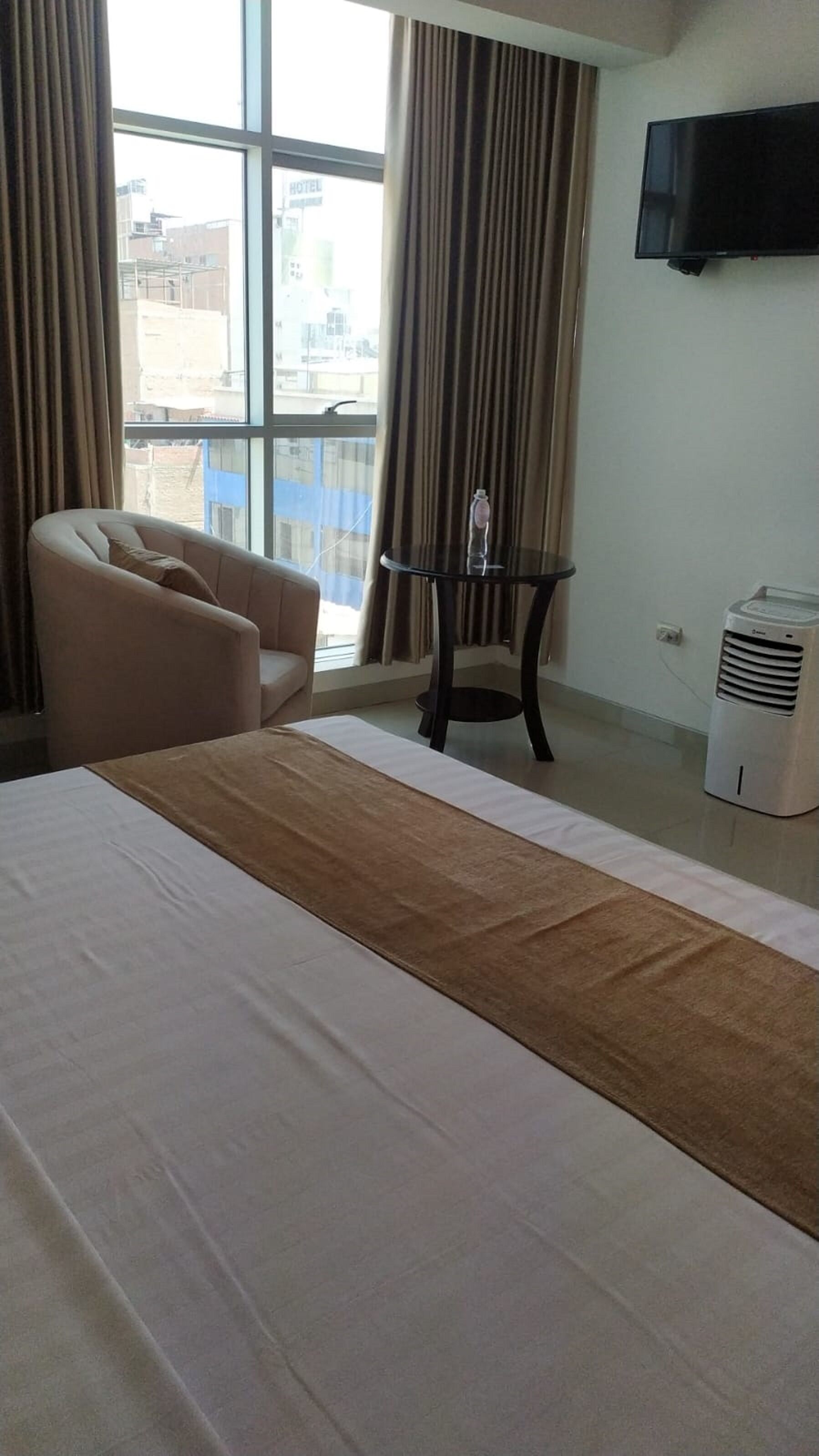 Quarto de hotel com uma cama grande, uma cadeira, uma mesa pequena com uma garrafa, uma TV e um aquecedor.