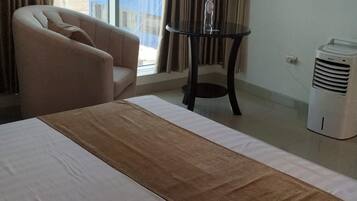 Quarto de hotel com uma cama grande, uma cadeira, uma mesa pequena com uma garrafa, uma TV e um aquecedor.