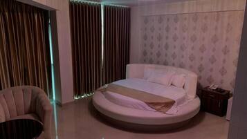 A circular bed in a modern bedroom with a chandelier, curtains, and a small bedside table.
