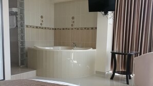 A hotel room with a large bed, a bathtub, a TV, and a chair.