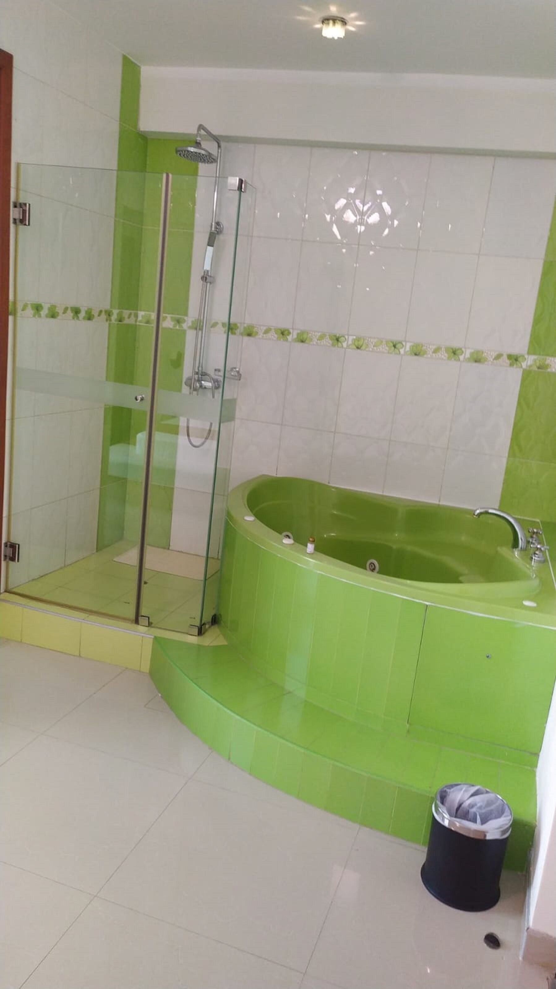 A bathroom with a glass-enclosed shower, a green bathtub, and white tiled walls.