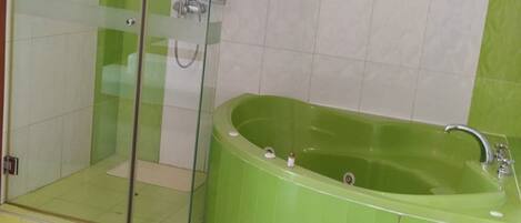 A bathroom with a glass-enclosed shower, a green bathtub, and white tiled walls.