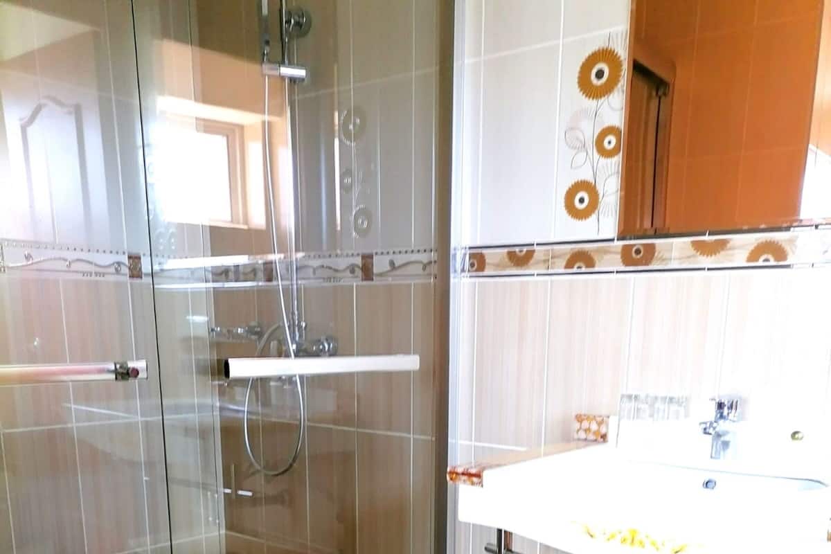 Une salle de bain moderne avec une douche à parois de verre, un lavabo blanc avec un miroir et un sol carrelé de couleur beige.