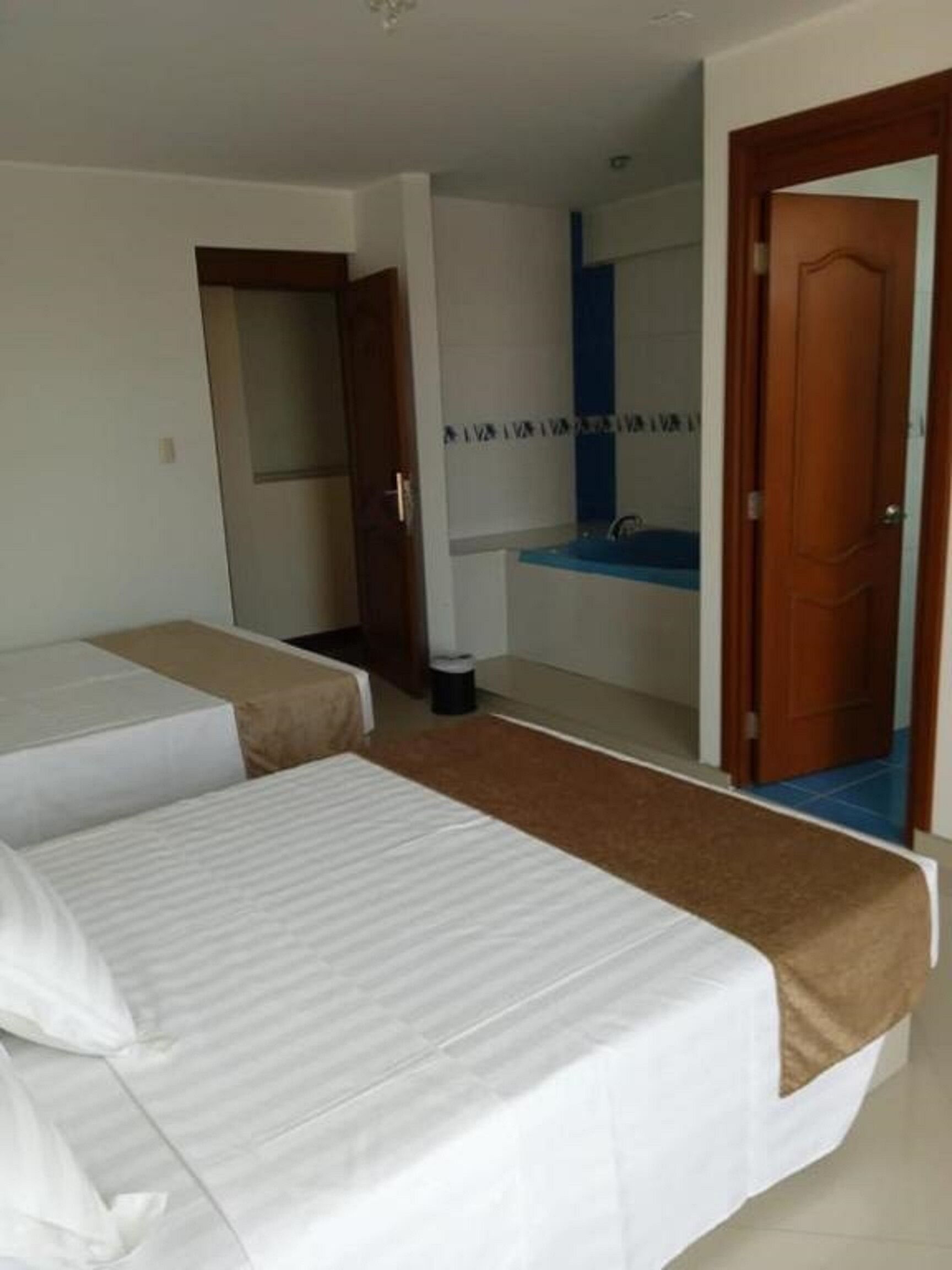 Habitación de hotel con dos camas individuales, baño con lavamanos azul y puerta que da a otra habitación.