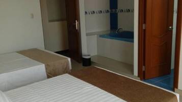 A hotel room with two single beds, a bathroom with a blue sink, and a door leading to another room.
