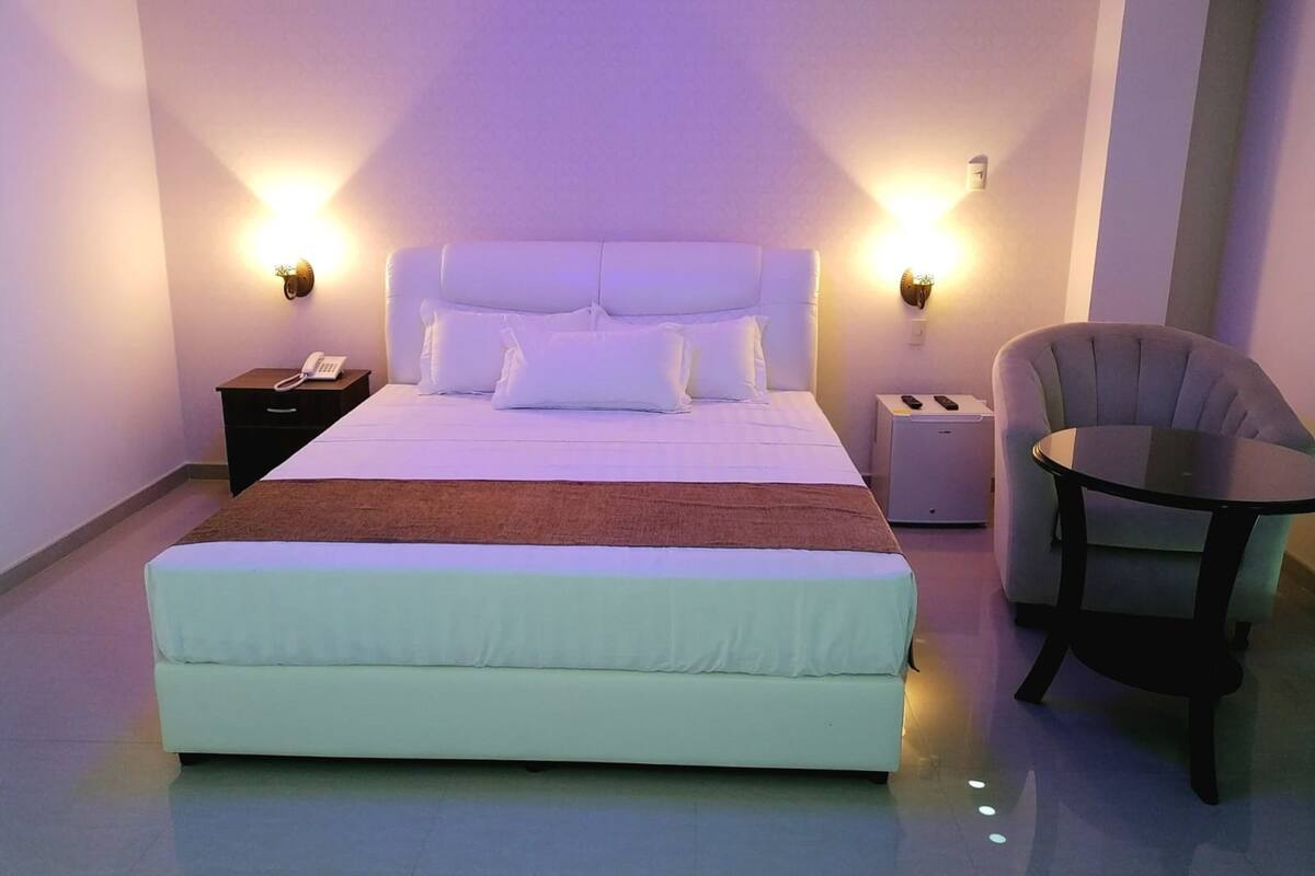 Une chambre d’hôtel moderne avec un grand lit, des lampes de chevet, un téléphone sur la table de chevet, une petite table et une chaise.