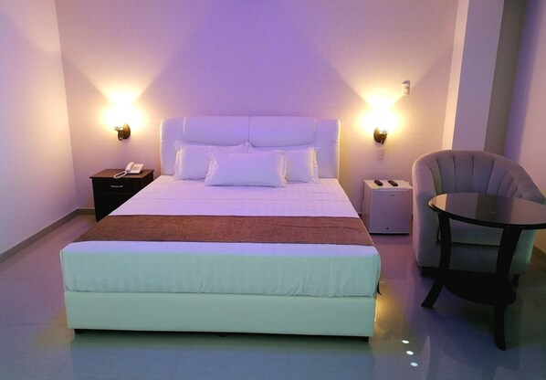 A modern hotel room with a large bed, bedside lamps, a bedside phone, a small table, and a chair.