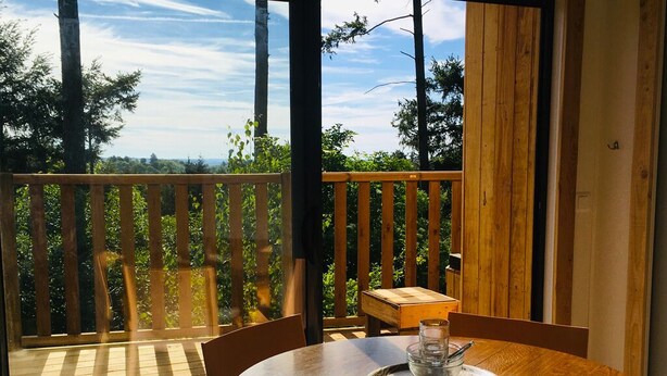 A wooden deck with a table and chairs, overlooking a forested area. - Chalet Le Coquet, cozy n'est surrounded by greenery - Naturist area (Collonges-la-Rouge)