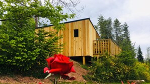 A wooden cabin with a deck, surrounded by greenery and a red rose in the foreground. - Chalet Le Coquet, cozy n'est surrounded by greenery - Naturist area (Collonges-la-Rouge)