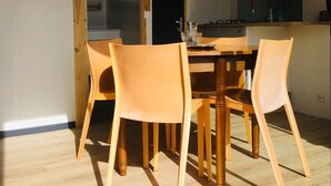 A dining area with a wooden table and four chairs, a kitchen area with a sink and cabinets, and a door leading to another room. - Chalet Le Coquet, cozy n'est surrounded by greenery - Naturist area (Collonges-la-Rouge)