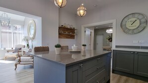 Una cocina moderna con una isla central, iluminación colgante y un reloj de pared grande.