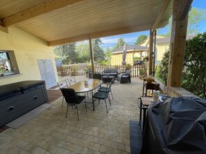 An outdoor patio with a wooden ceiling, a table with chairs, a barbecue grill, and a covered seating area. - In the heart of Auvergne: a family home with a swimming pool in the countryside, offering every comfort (Joze)