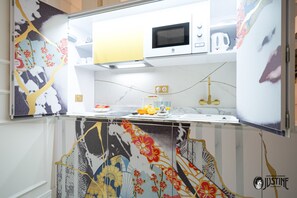 A kitchen with a microwave, kettle, and fruit bowl.