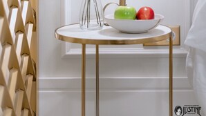 A white wall with a decorative panel, a white vase with branches and a bowl of fruit, and a white lamp.
