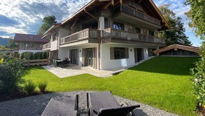 A two-story chalet with a balcony, a patio with outdoor furniture, and a well-maintained lawn. - Apartment SeeSuite 2 (Rottach-Egern)