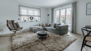 A modern living room with a grey sofa, a brown armchair, a round coffee table, and a fluffy rug. - Apartment SeeSuite 2 (Rottach-Egern)