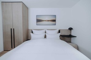 Quarto com uma cama grande, guarda-roupa, mesa de cabeceira e um quadro na parede.