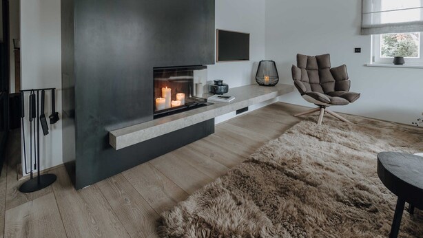 A modern living room with a fireplace, a comfortable armchair, and a large furry rug. - Apartment SeeSuite 2 (Rottach-Egern)