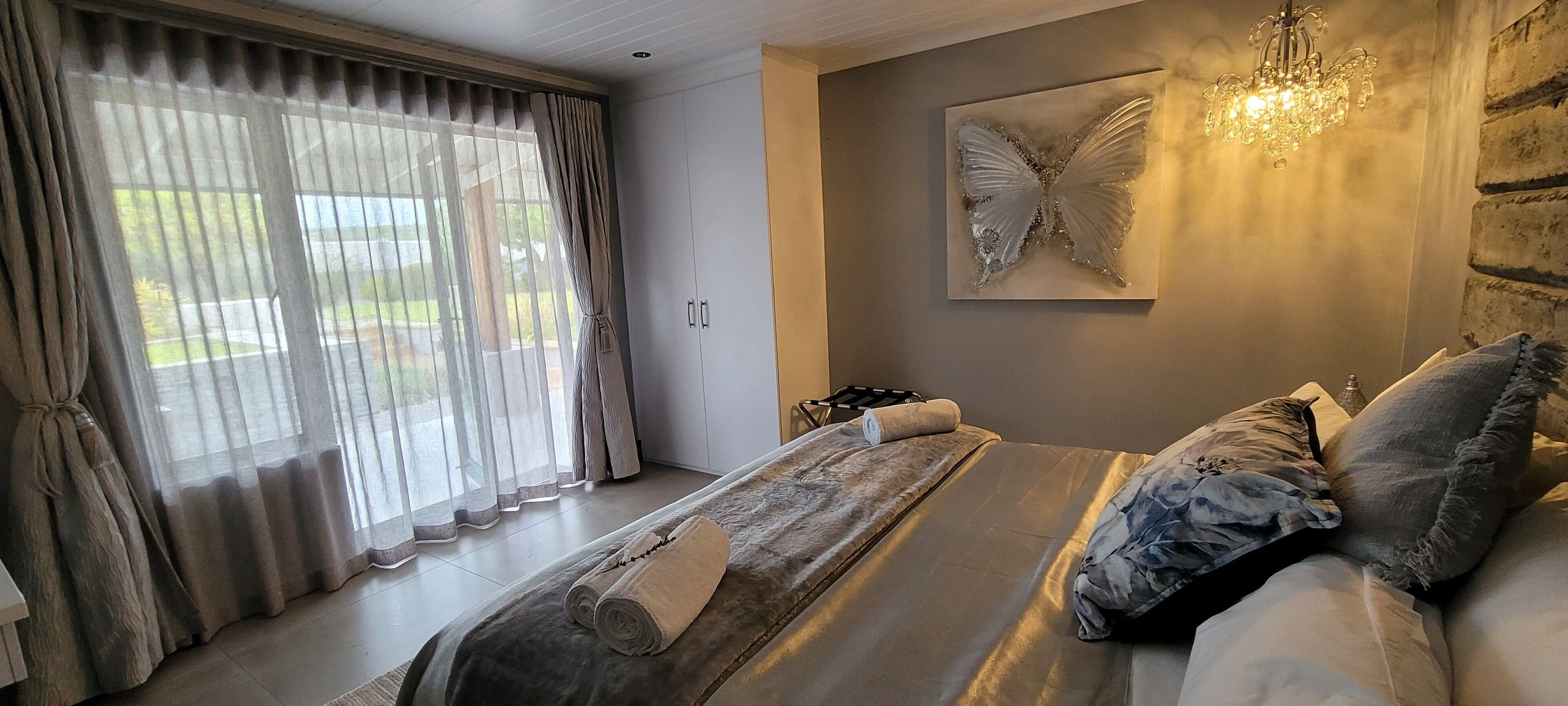Una camera da letto con un letto grande, un lampadario, un quadro decorativo a forma di farfalla e vista dalla finestra.