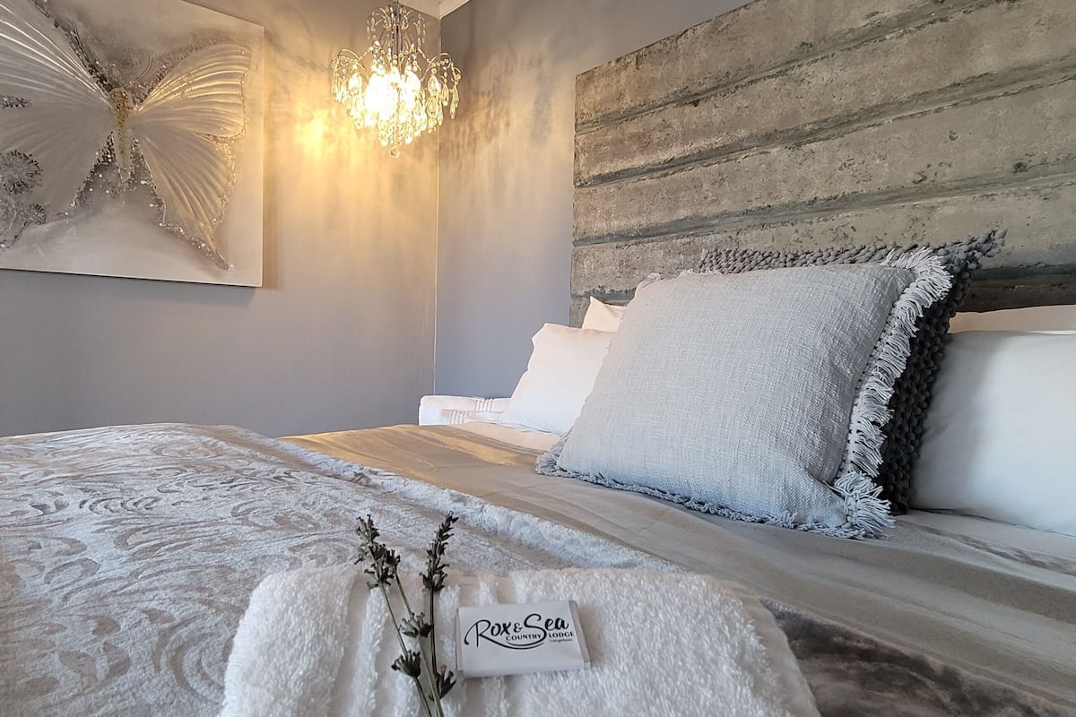 A neatly made bed with a white duvet and pillows, a decorative butterfly artwork on the wall, and a chandelier.