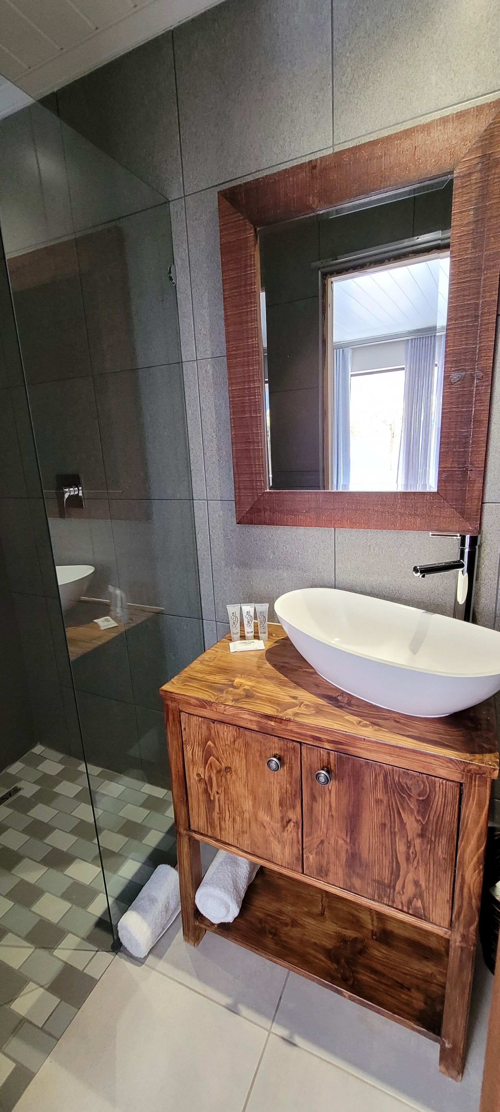 Un baño con tocador de madera, lavamanos blanco y espejo grande.