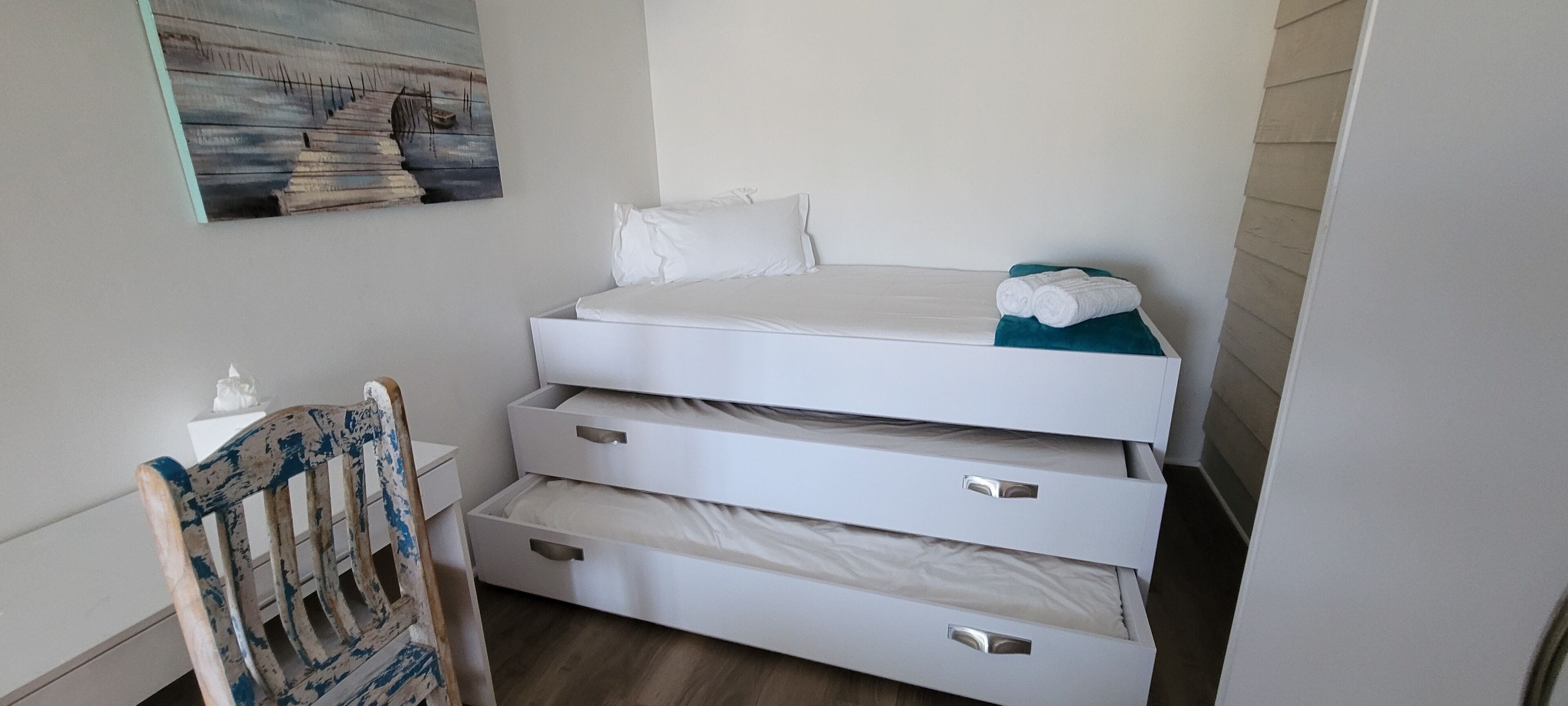 Un dormitorio pequeño con cama, una silla y una obra de arte colgada en la pared.