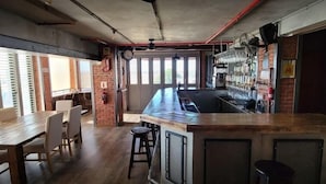 A bar area with a long counter, stools, and a brick wall. - Rox and Sea Country Lodge (Langebaan)