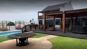 A modern outdoor patio with a pool, wooden deck, and seating areas. - Rox and Sea Country Lodge (Langebaan)