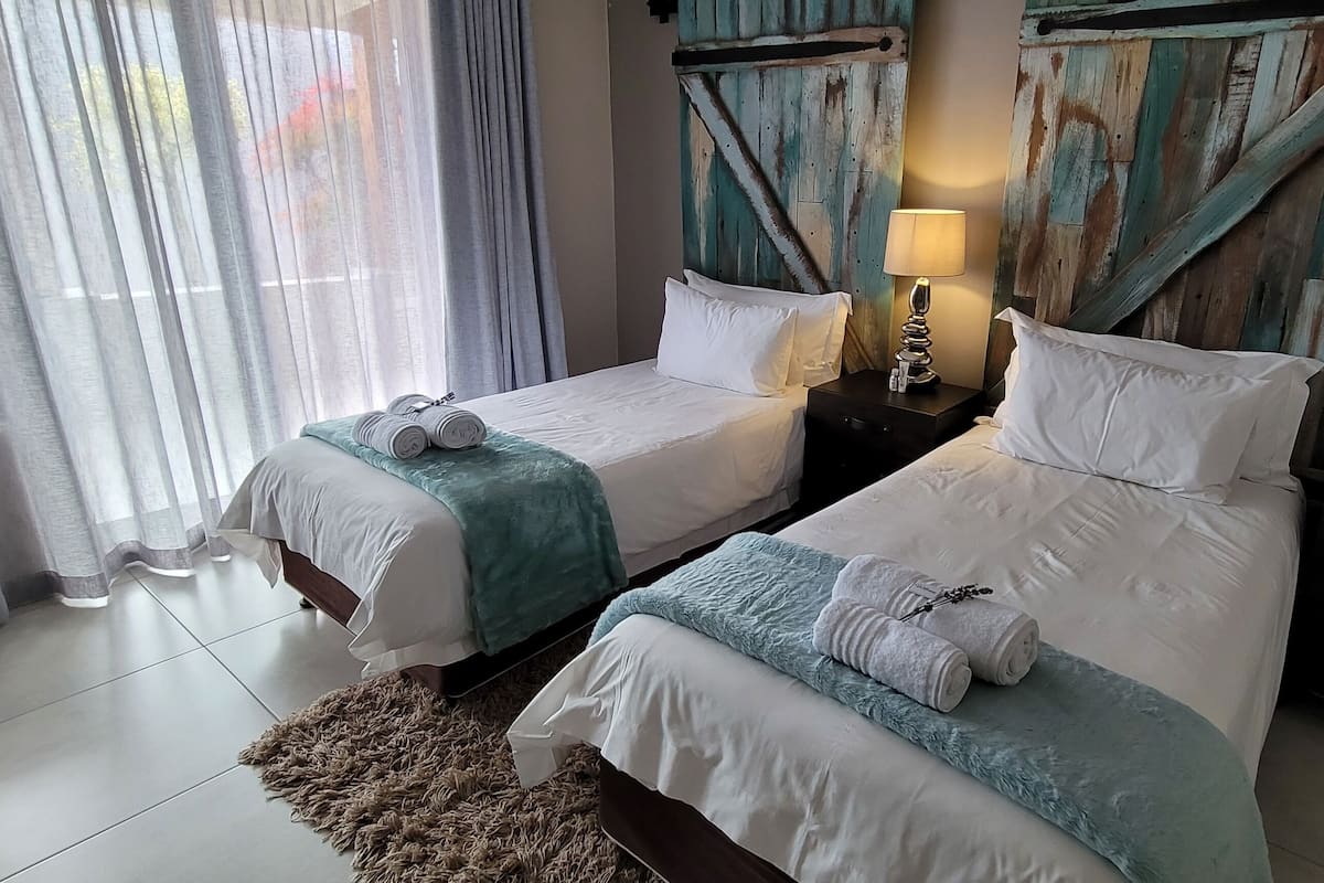 A hotel room with two beds, a wooden headboard, a lamp, and a small table with a lantern.