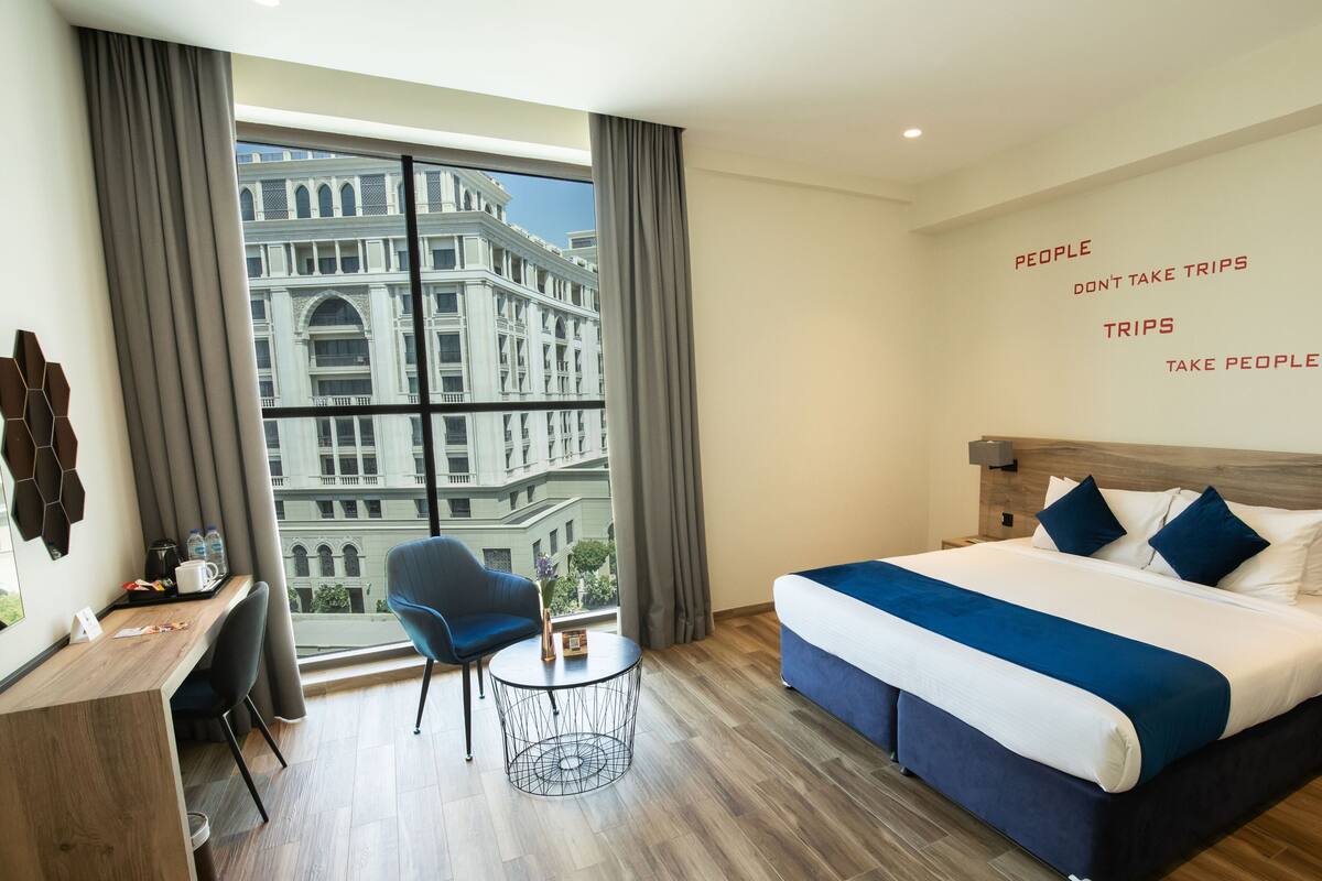Une chambre d’hôtel avec un grand lit, un bureau, une chaise et une vue sur un immeuble par la fenêtre.
