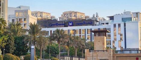 A modern hotel with a prominent sign in Arabic, surrounded by palm trees and a water body.
