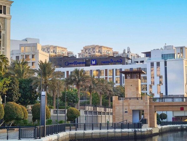 Een modern hotel met een opvallend bord in Arabisch, omgeven door palmbomen en een waterpartij.