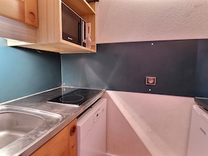 Una cocina compacta con un lavamanos de acero inoxidable, horno empotrado, lavavajillas y armarios de madera.