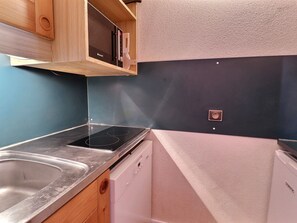 A compact kitchen with a stainless steel sink, a built-in oven, a dishwasher, and wooden cabinetry.