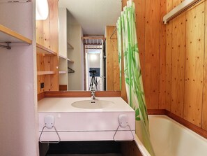 A bathroom with wooden paneling, a white sink, and a green shower curtain.