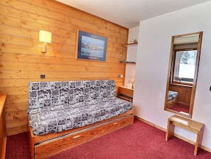A wooden-paneled room with a bed, a small table, a mirror, and a framed picture on the wall.