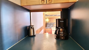 Una kitchenette con cafetera y tetera sobre una encimera azul, armarios de madera arriba y vistas a un espacio con baldosas estampadas.