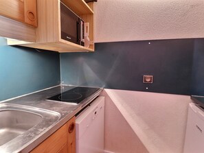 A compact kitchen with a stainless steel sink, a built-in oven, a dishwasher, and wooden cabinetry.