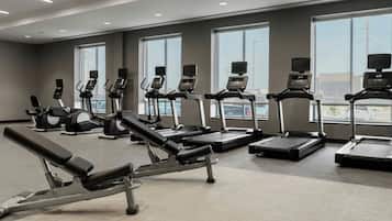 A gym with various exercise equipment, large windows, and a view of the outside.