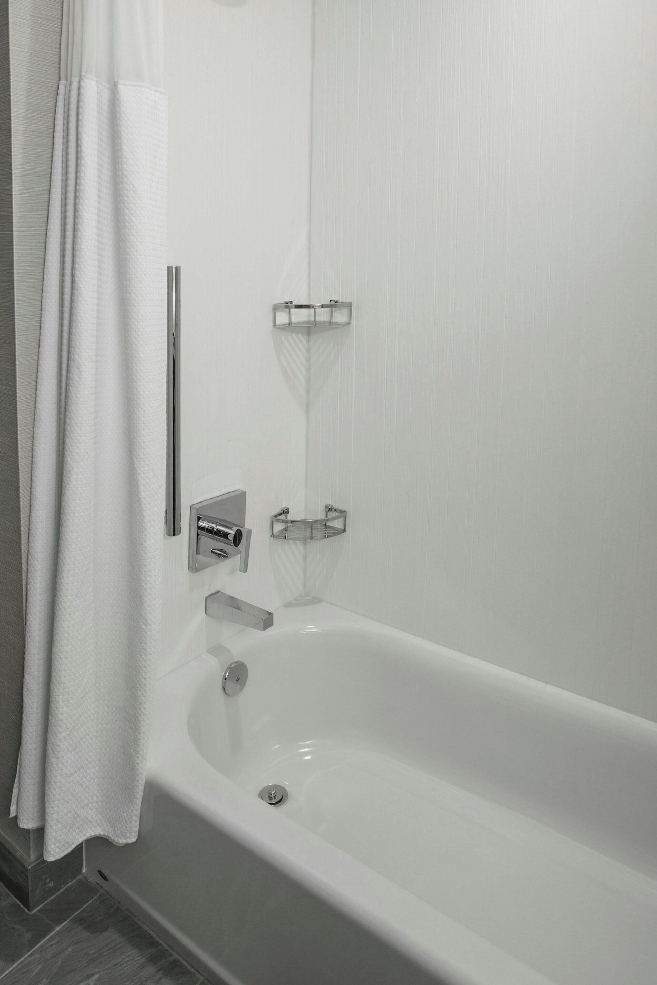 A modern bathroom with a white bathtub, a towel rack, and a shower curtain.