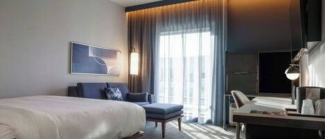 A modern hotel room with a large bed, a desk, a chair, and a TV.