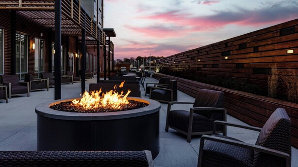 An outdoor seating area with a circular fire pit, wicker chairs, and a brick wall. - Courtyard by Marriott Indianapolis Fishers (Fishers)