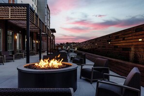 An outdoor seating area with a circular fire pit, wicker chairs, and a brick wall. - Courtyard by Marriott Indianapolis Fishers (Fishers)