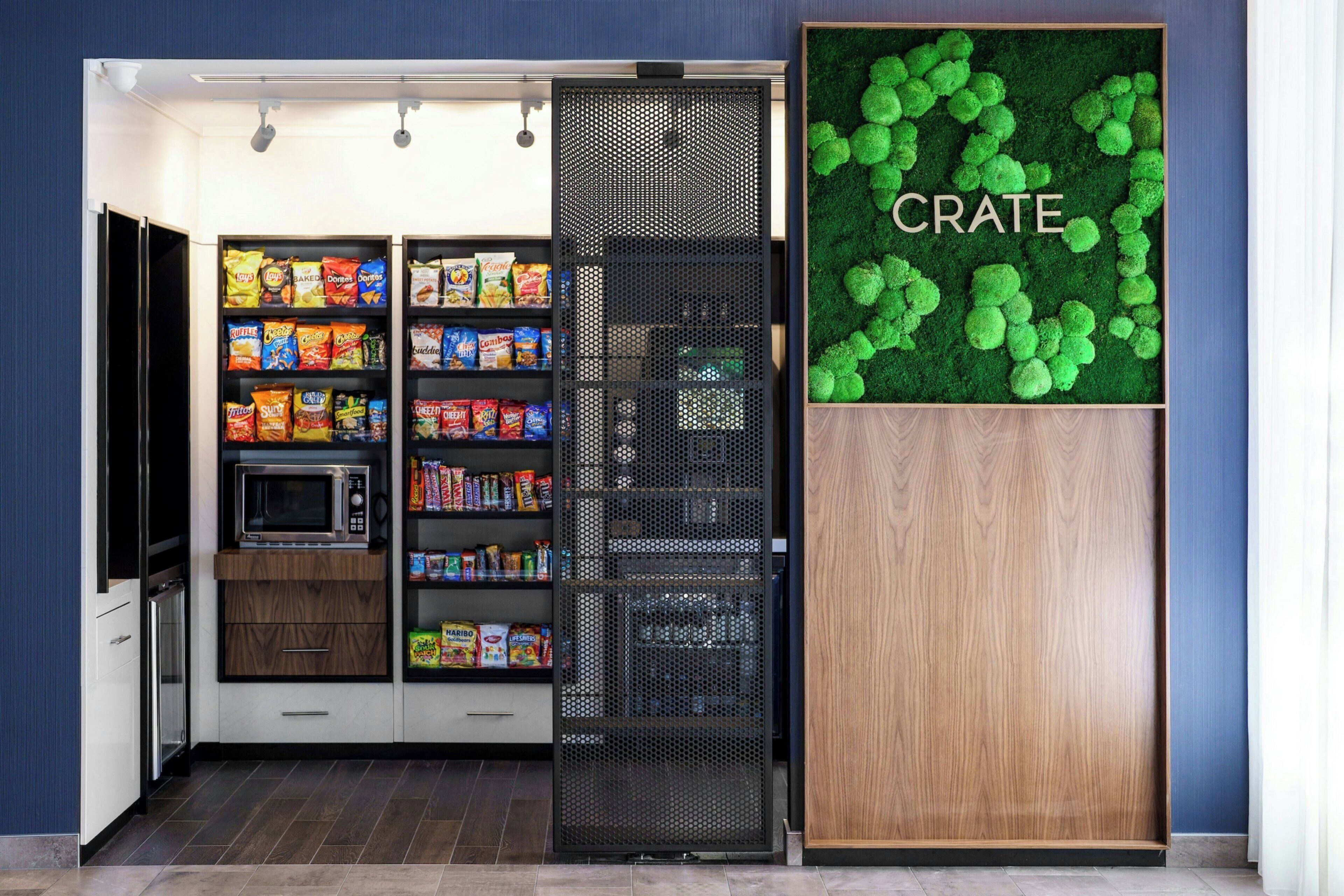 A compact kitchenette with a microwave, shelves of snacks, and a decorative green wall with the word "CRATE".