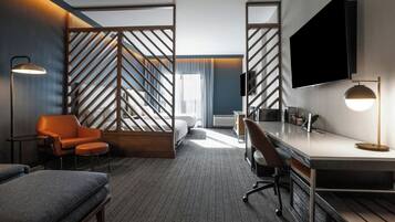 A modern hotel room with a large bed, a desk, a chair, a sofa, and a TV.