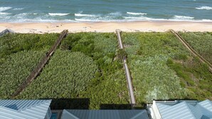 An aerial view of a beach with a wooden boardwalk leading to the shore, surrounded by dense vegetation. - Coastal Heaven by Distinctive Beach Rentals (Palm Coast)