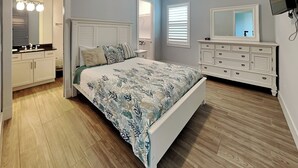 A bedroom with a bed, dresser, and a TV mounted on the wall. - Coastal Heaven by Distinctive Beach Rentals (Palm Coast)